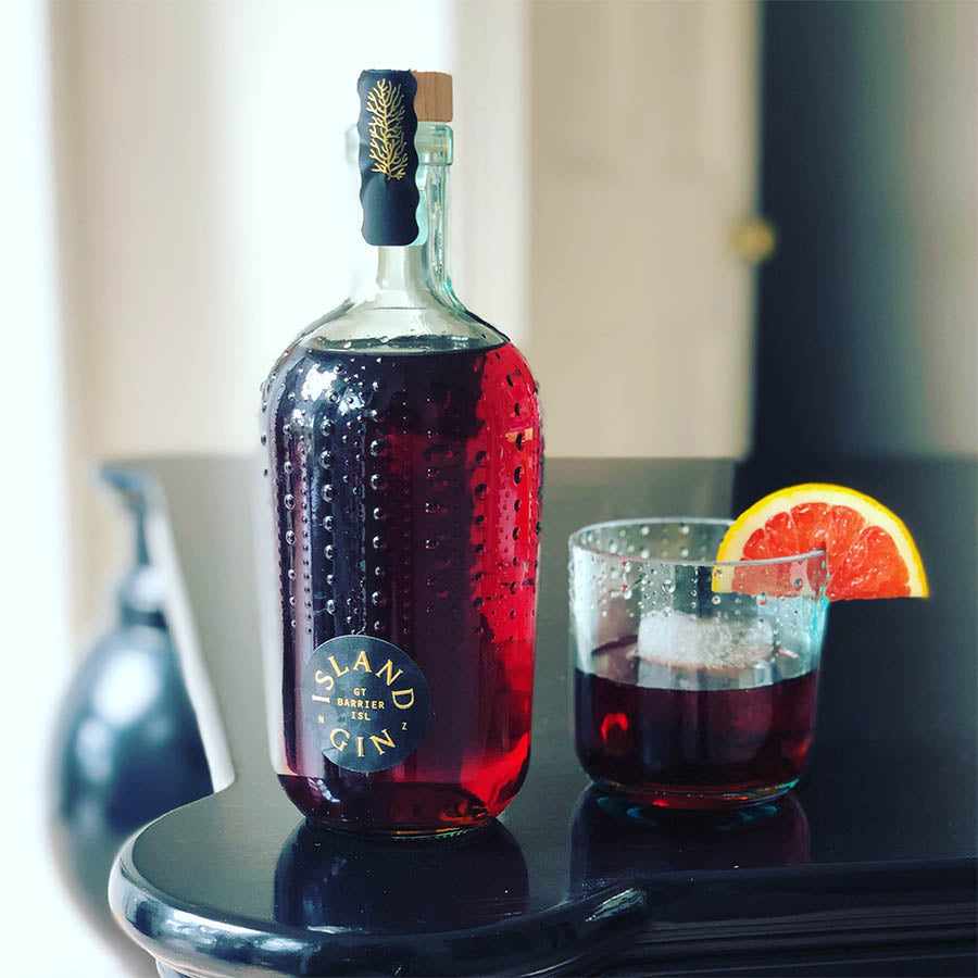 Island Gin Negroni in a bottle sitting next to a glass with a blood orange slice.